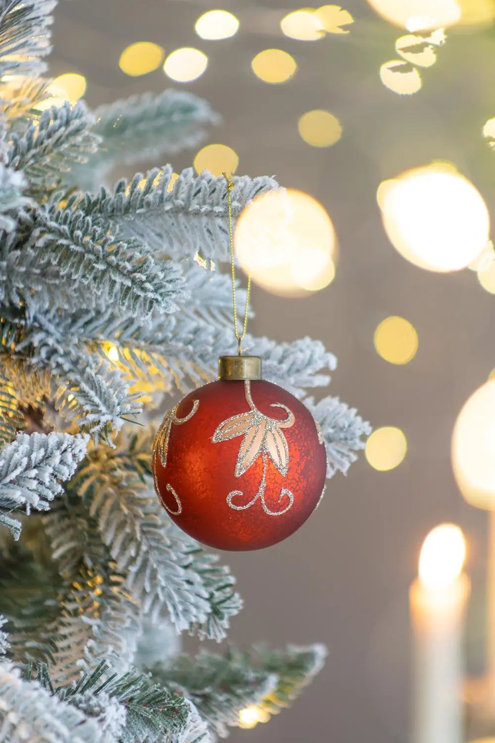 Red Christmas ball ornament with gold glitter leaf design hanging on frosted pine branch on Tampa Home & Garden Store