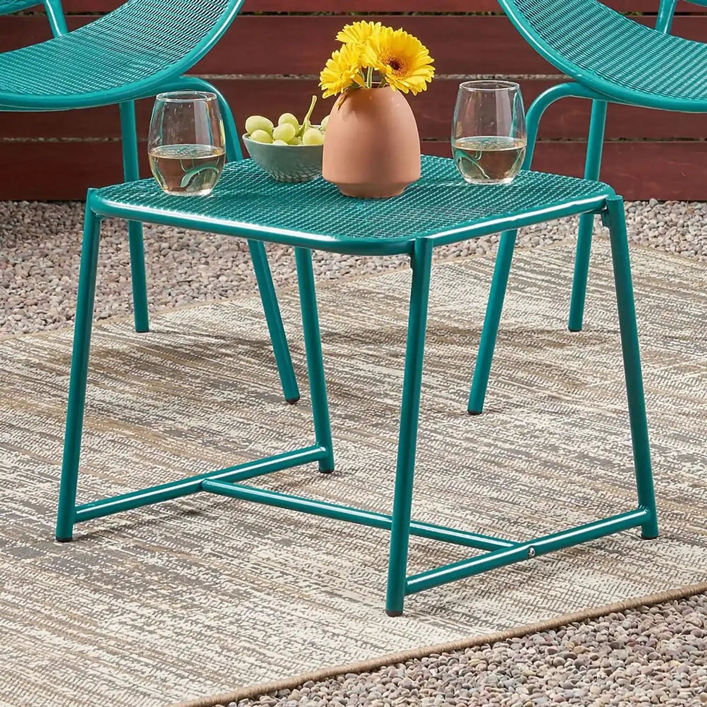 Two teal outdoor iron chairs with mesh seats around a teal mesh table with a yellow flower vase on Tampa Home & Garden Store
