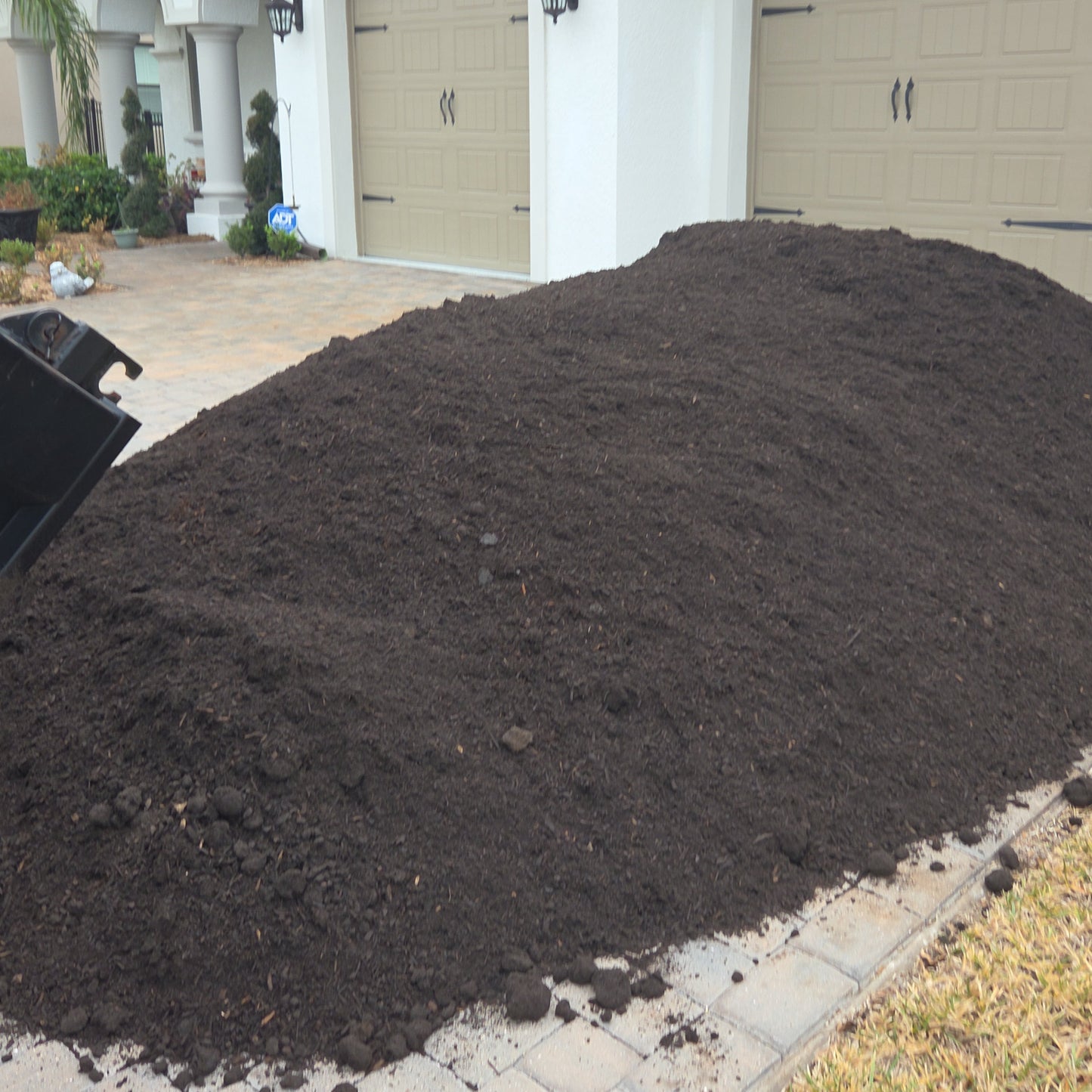 9 cubic yard pile of dark topsoil in front of a house with beige doors.