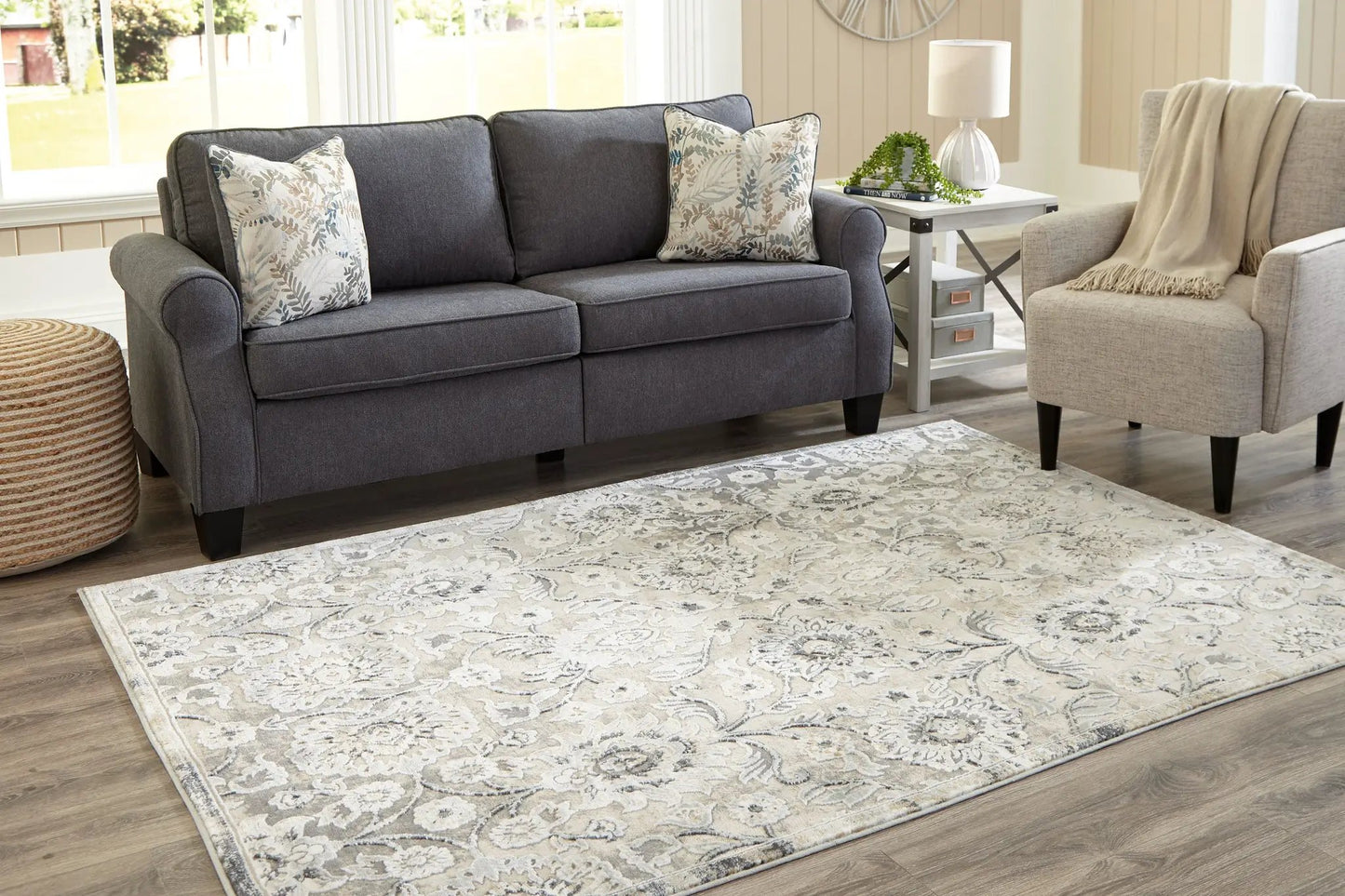 Kilkenny area rug in ivory and gray with floral motif on light wood floor beside gray sofa on Tampa Home & Garden Store