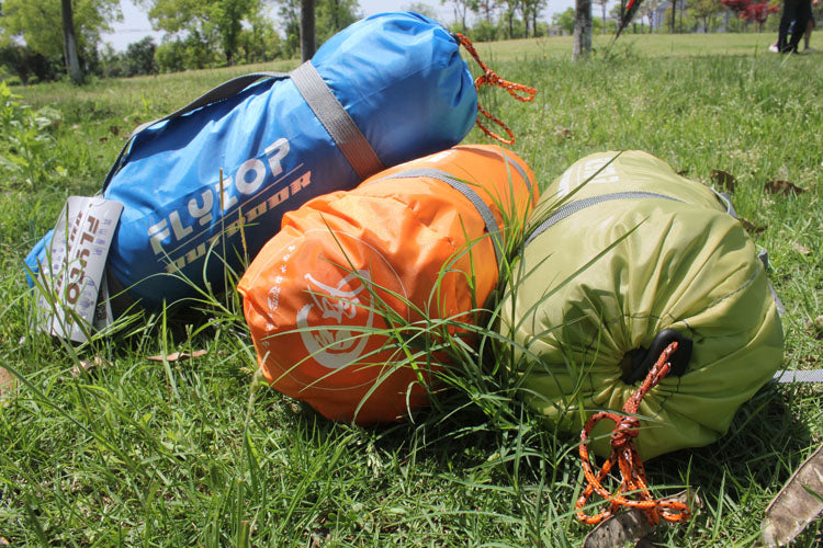 Three color coded camping gear sacks in blue orange and green with drawstrings on grass field on Tampa Home & Garden Store