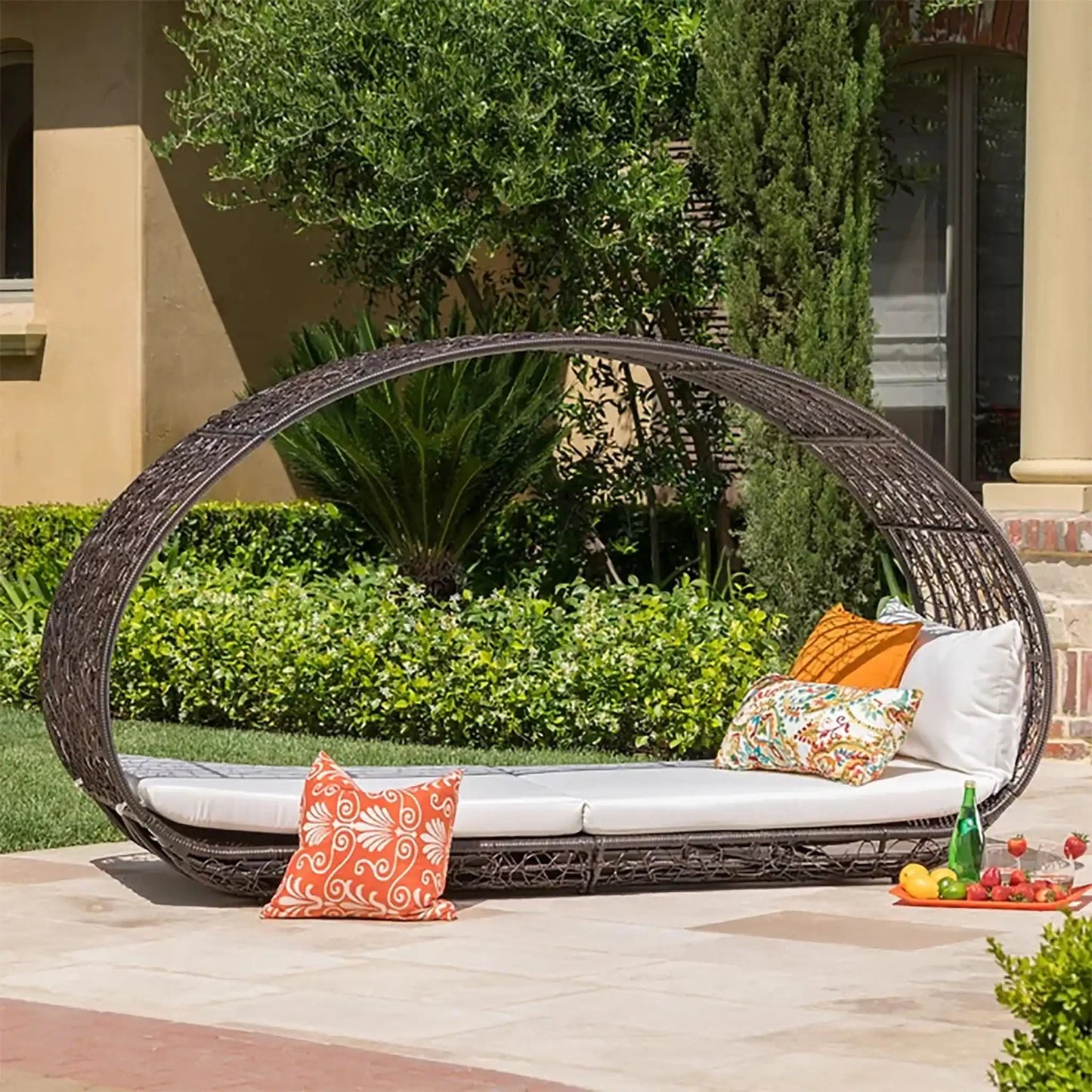 Abigal Outdoor Wicker Daybed Cushions with white cushions and orange pillows in a lush courtyard on Tampa Home & Garden Store