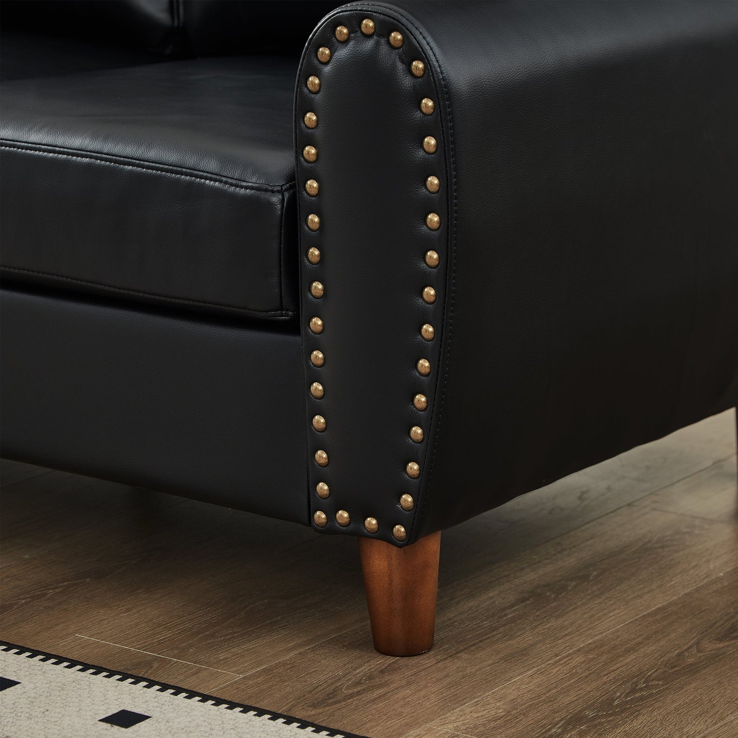 Black faux-leather loveseat arm close-up with brass nailhead trim and a dark wood leg on Tampa Home & Garden Store