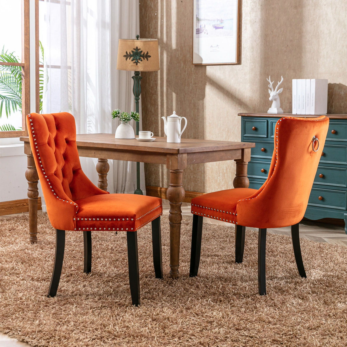 Tufted velvet dining chairs with nailhead trim in orange, pair around a wooden dining table on Tampa Home & Garden Store
