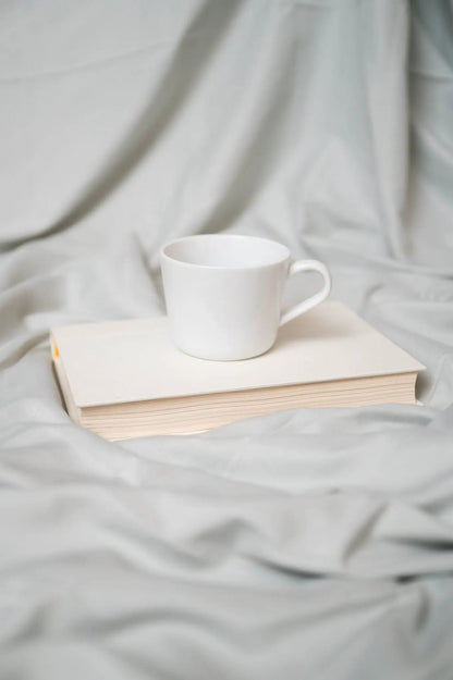 White ceramic mug on a stack of books resting on soft gray fabric backdrop on Tampa Home & Garden Store