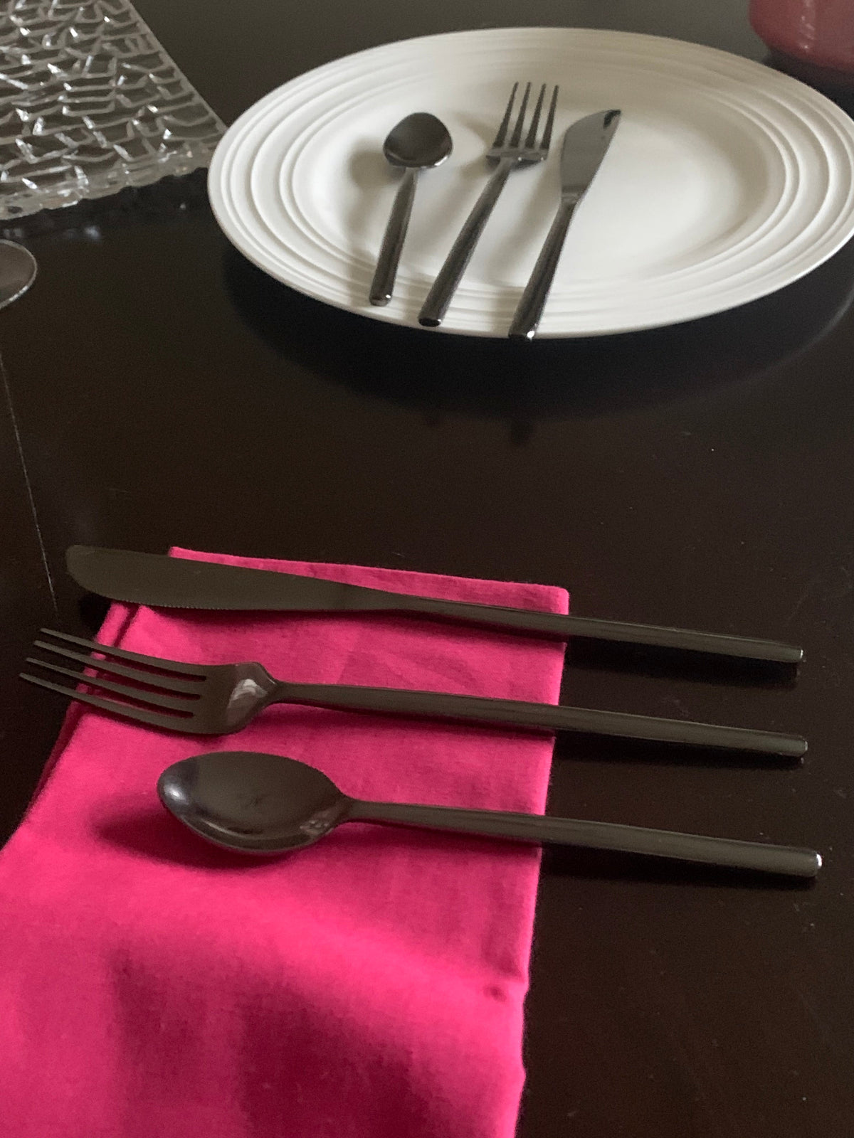 Vibhsa 18 pc flatware set matte black stainless steel on pink napkin with white plates on Tampa Home & Garden Store