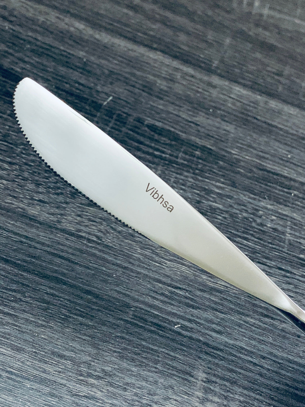 Vibhsa knife blade close-up with serrated edge and logo on dark wood surface on Tampa Home & Garden Store