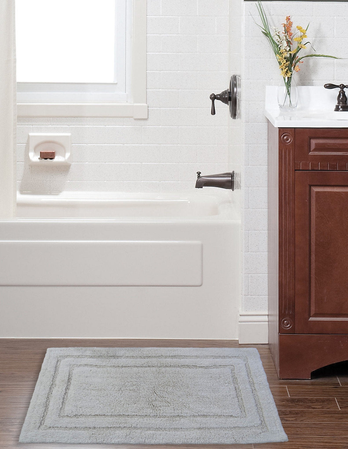 Vibhsa ivory bath rug 20x32 in front of bathtub with white tile and vanity, bordered plush mat on Tampa Home & Garden Store