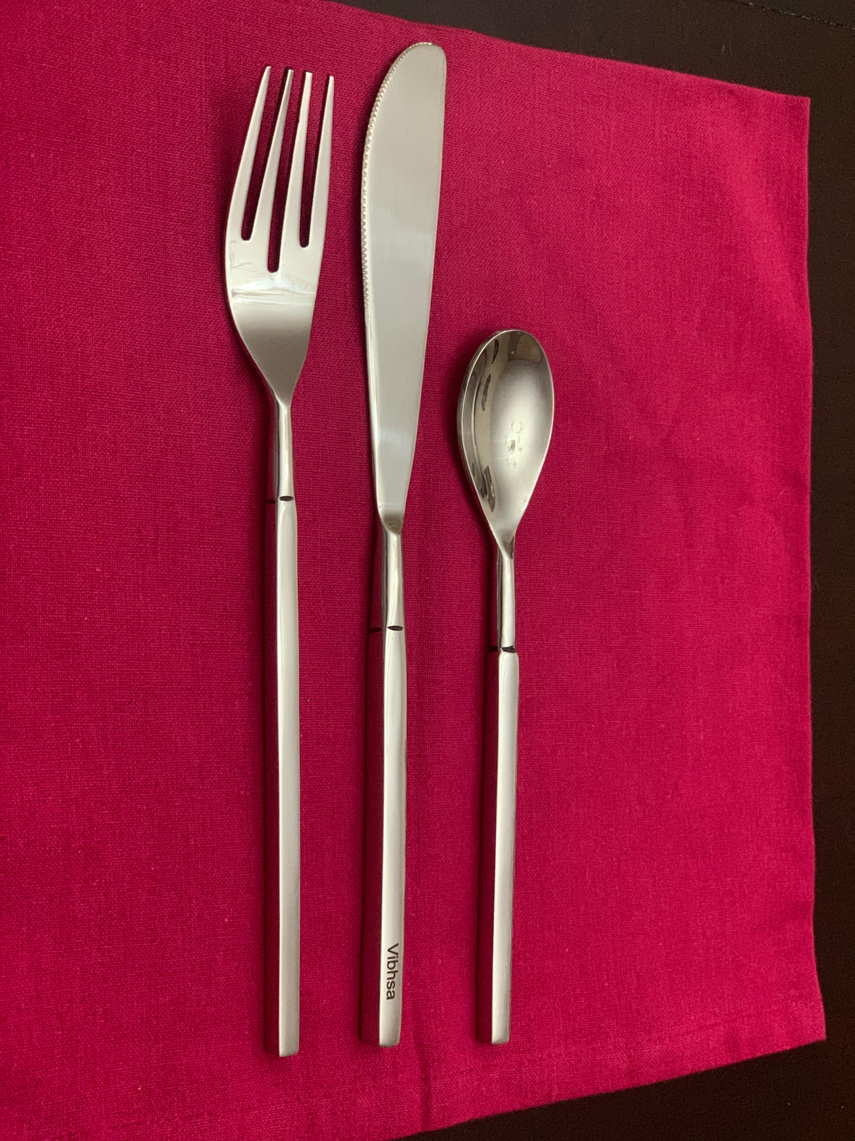 Vibhsa flatware trio: dinner fork, dinner knife, dessert spoon in polished stainless steel on pink cloth on Tampa Home & Garden Store