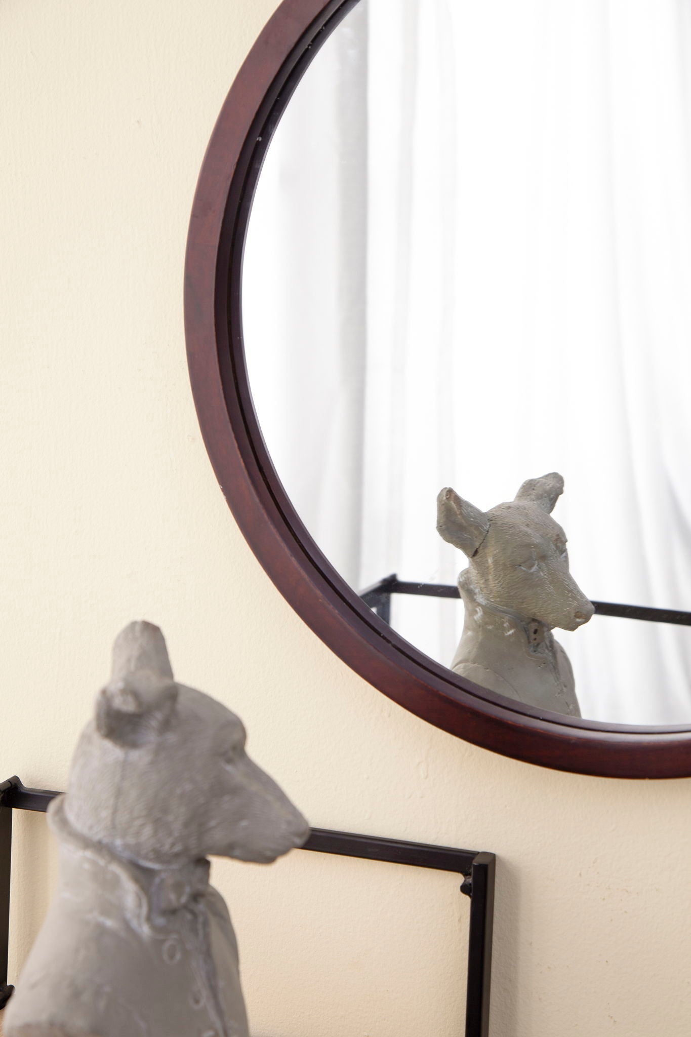 Circle wall mirror with dark wooden frame above a shelf with gray sculpture figurines on Tampa Home & Garden Store