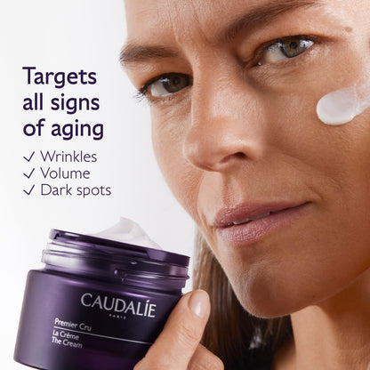 Caudalie Premier Cru Rich Cream jar in deep purple beside a model's face with cream on cheek on Tampa Home & Garden Store
