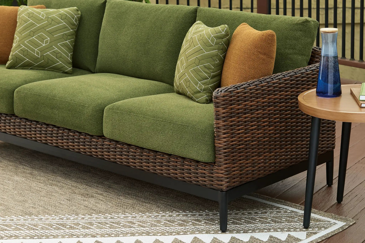 Horizon Hall sofa in green fabric with wicker base and brown pillow; cushions add color on Tampa Home & Garden Store