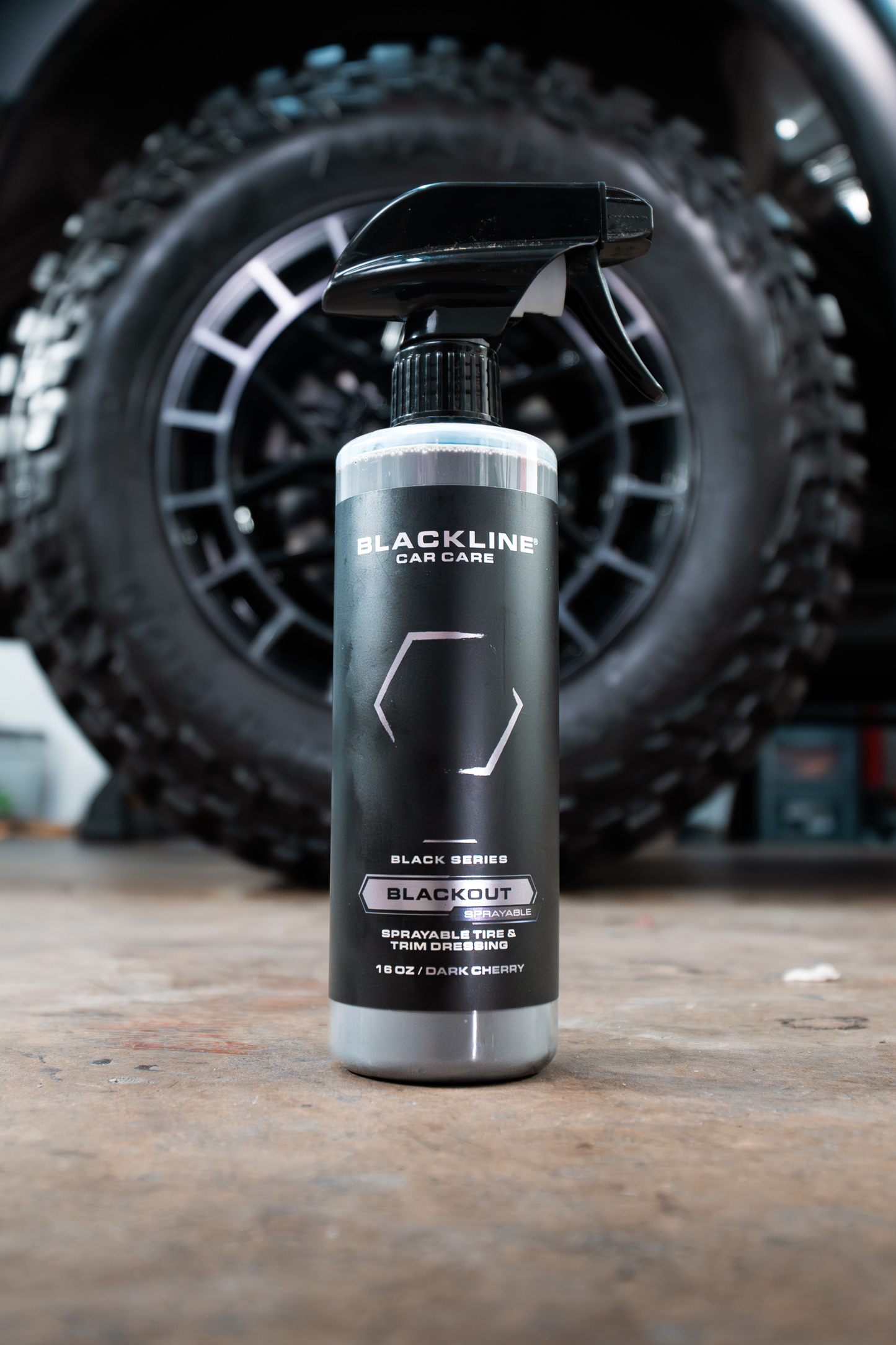 Blackline Car Care Blackout tire and trim dressing spray bottle in front of a tire on Tampa Home & Garden Store