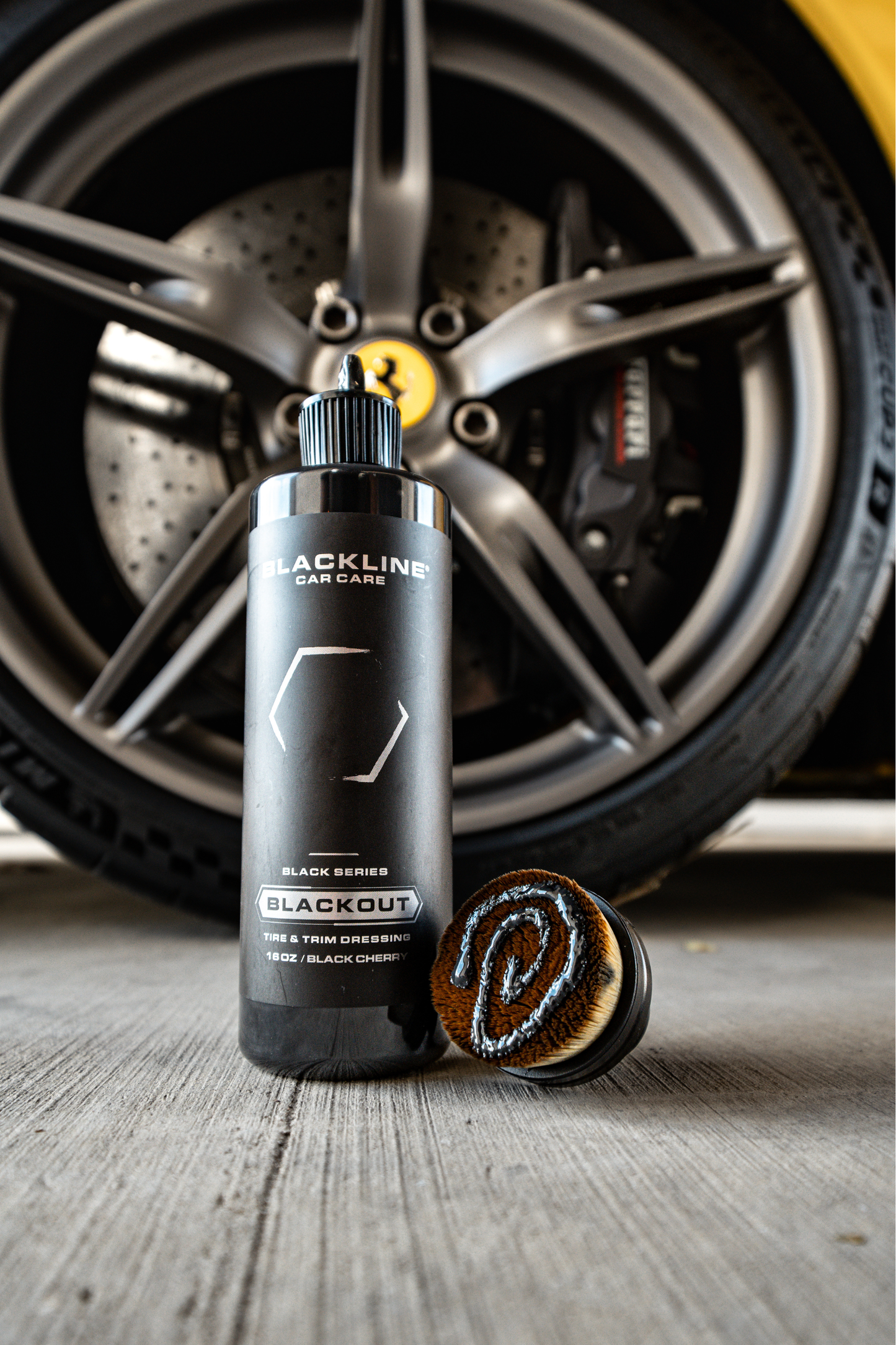 Blackline Car Care Blackout Tire & Trim Dressing bottle in front of a car wheel and brake rotor on Tampa Home & Garden Store