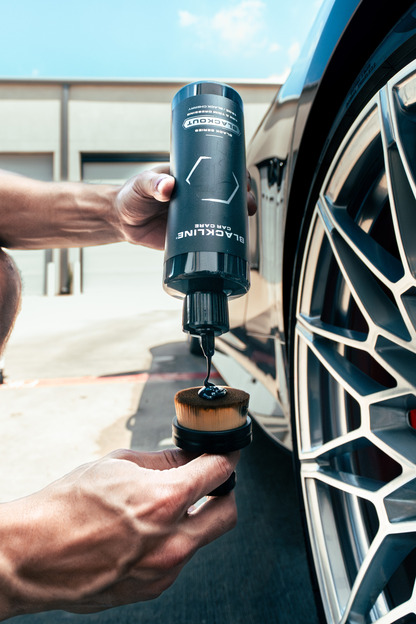 Blackline Blackout Trim & Tire Dressing bottle beside a car wheel, dark gray container on Tampa Home & Garden Store