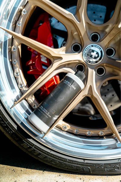 BLACKLINE BLACKOUT TRIM & TIRE DRESSING bottle beside a gold alloy wheel with red brake calipers on Tampa Home & Garden Store