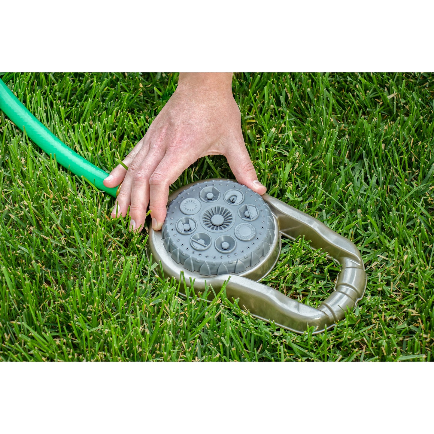 Metal 8-pattern lawn sprinkler on weighted base with hand on gray top beside green hose on Tampa Home & Garden Store