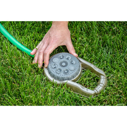 Metal 8-pattern lawn sprinkler on weighted base with hand on gray top beside green hose on Tampa Home & Garden Store