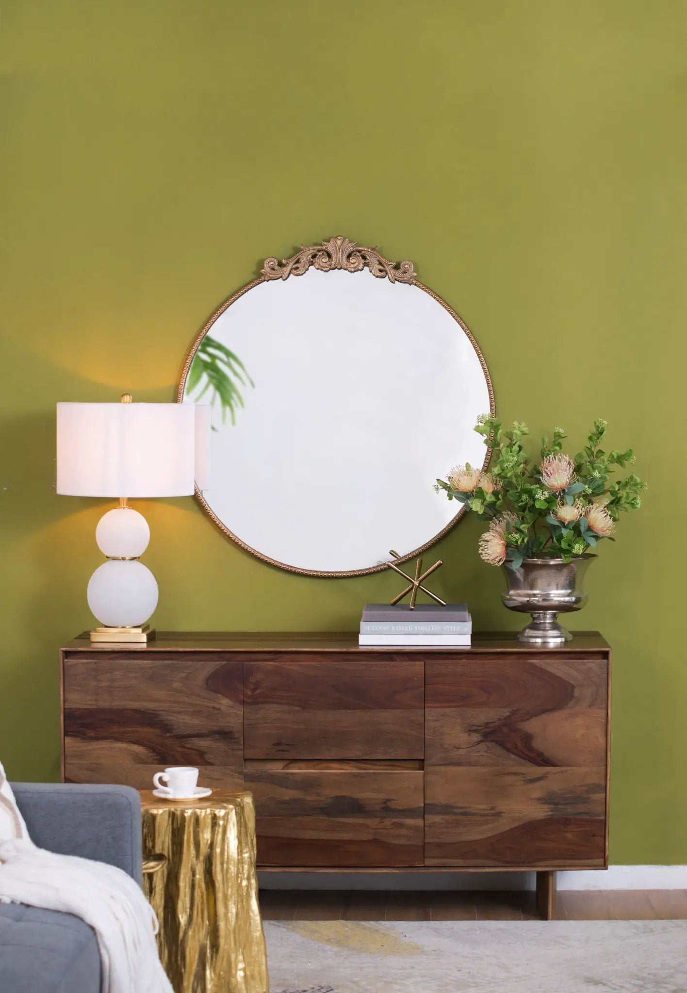 Round wall mirror with ornate baroque frame leaning against a green wall above a wooden console on Tampa Home & Garden Store