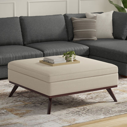 Beige fabric storage ottoman with lift-top, wooden legs, tray of books and a plant on top on Tampa Home & Garden Store