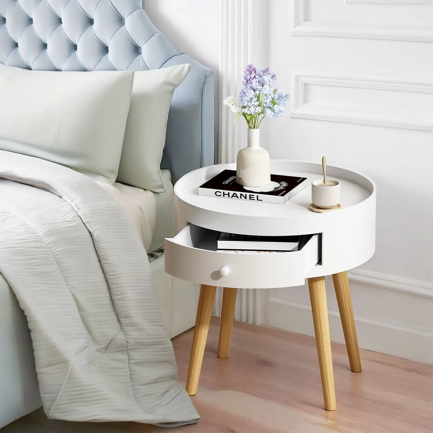 White round nightstand with storage drawer on wood legs, topped with a vase and Chanel book on Tampa Home & Garden Store