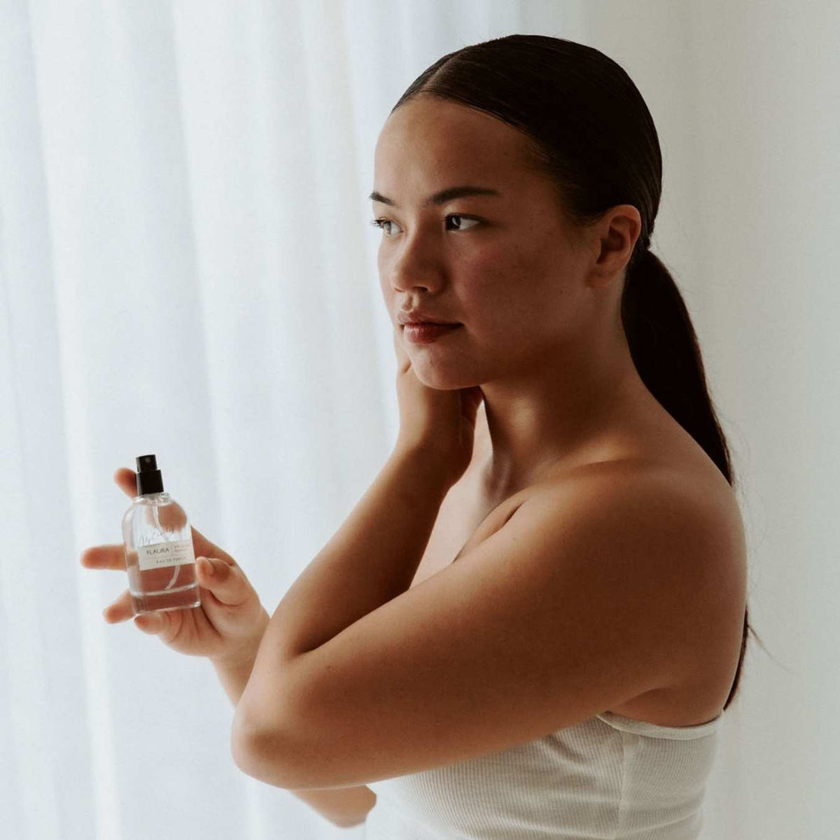 Flaura Eau De Parfum bottle by UpCircle, clear glass with black spray cap held by a woman on Tampa Home & Garden Store