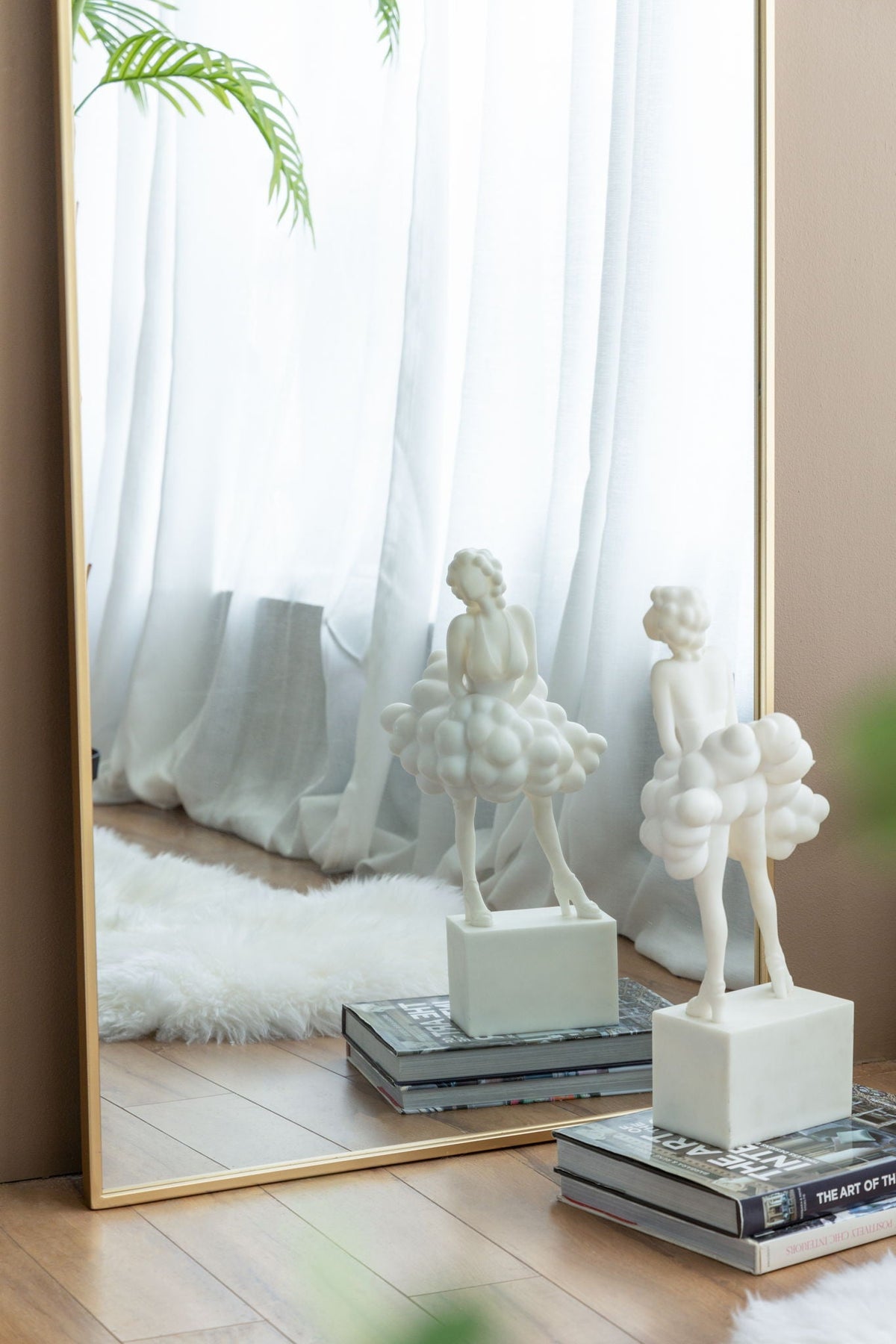 Celine Arch Body Mirror with slim gold frame leaning against beige wall, reflects curtains and a palm plant on Tampa Home & Garden Store