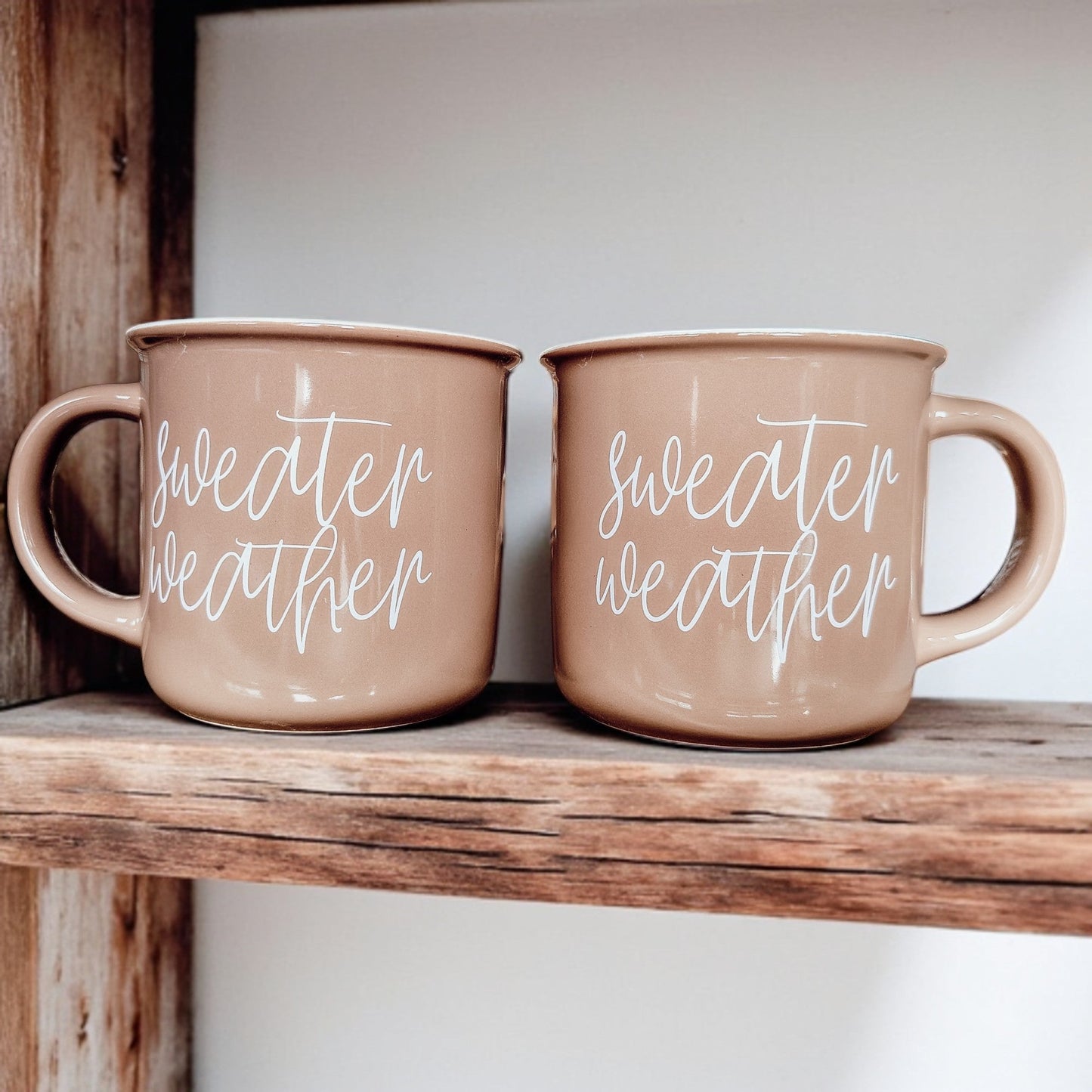 Two Gia Roma Sweater Weather coffee mugs in dusty-pink with white script on a wood shelf on Tampa Home & Garden Store