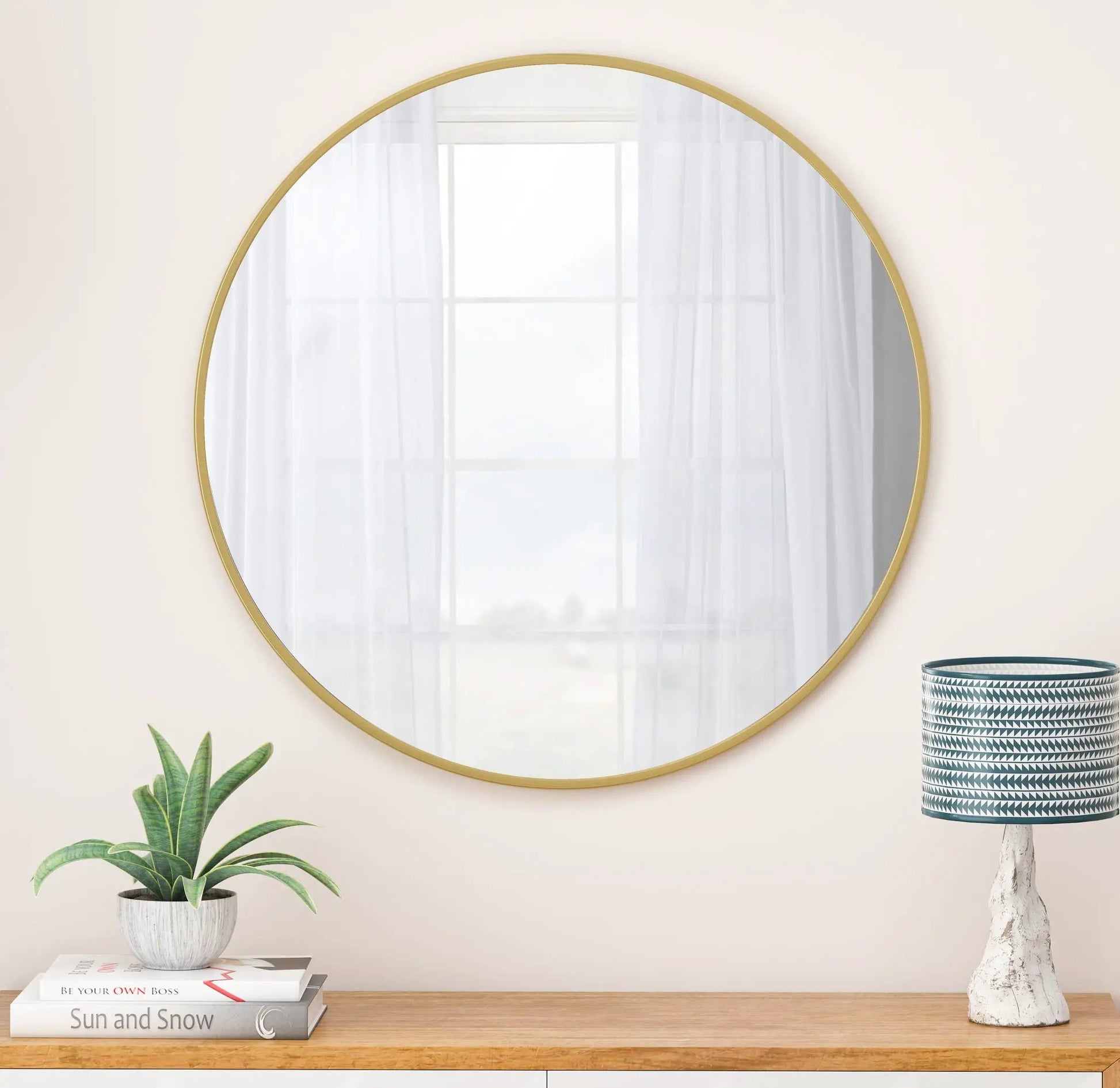 Wall circular mirror with a gold metal frame on beige wall reflecting a window on Tampa Home & Garden Store