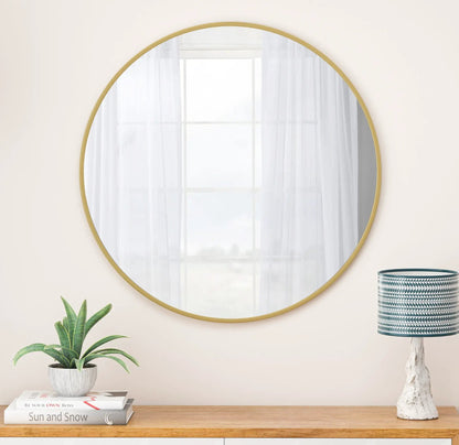 Wall circular mirror with a gold metal frame on beige wall reflecting a window on Tampa Home & Garden Store