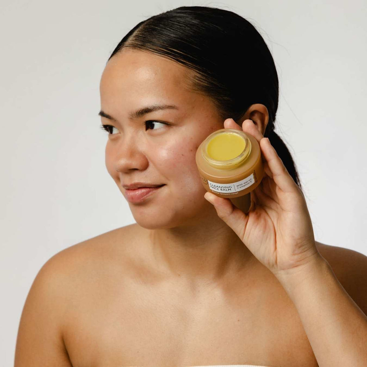 UpCircle Cleanse, Tone + Moisturize Set cleansing balm in a tan jar with yellow balm held near a woman's face on Tampa Home & Garden Store