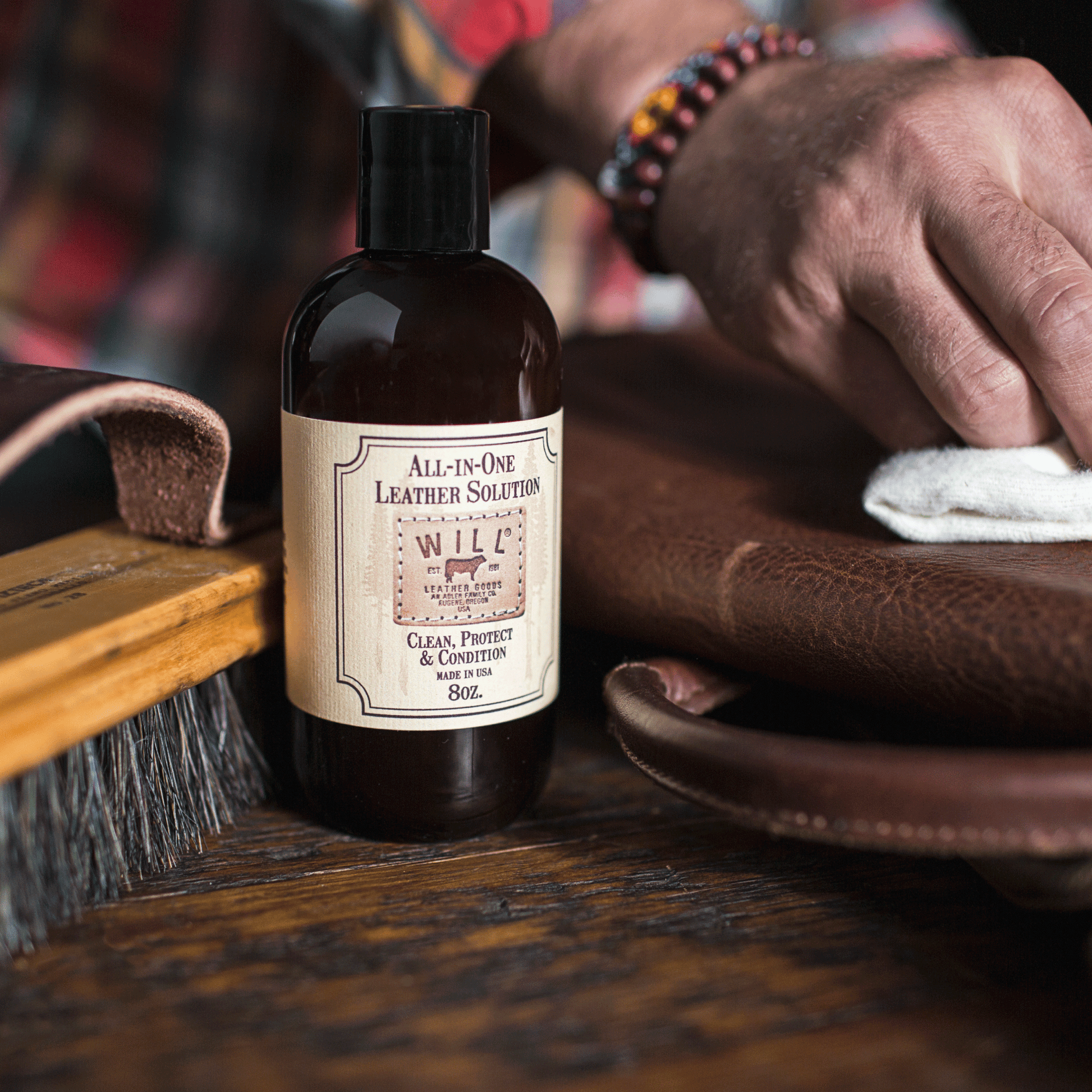 All-In-One Leather Solution bottle with Will Leather Goods label beside a leather cleaning brush and brown leather on Tampa Home & Garden Store