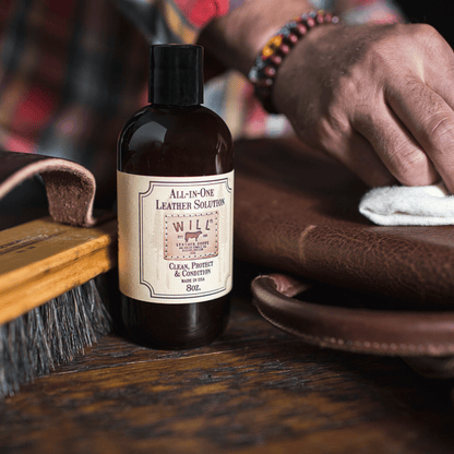 All-In-One Leather Solution bottle with Will Leather Goods label beside a leather cleaning brush and brown leather on Tampa Home & Garden Store