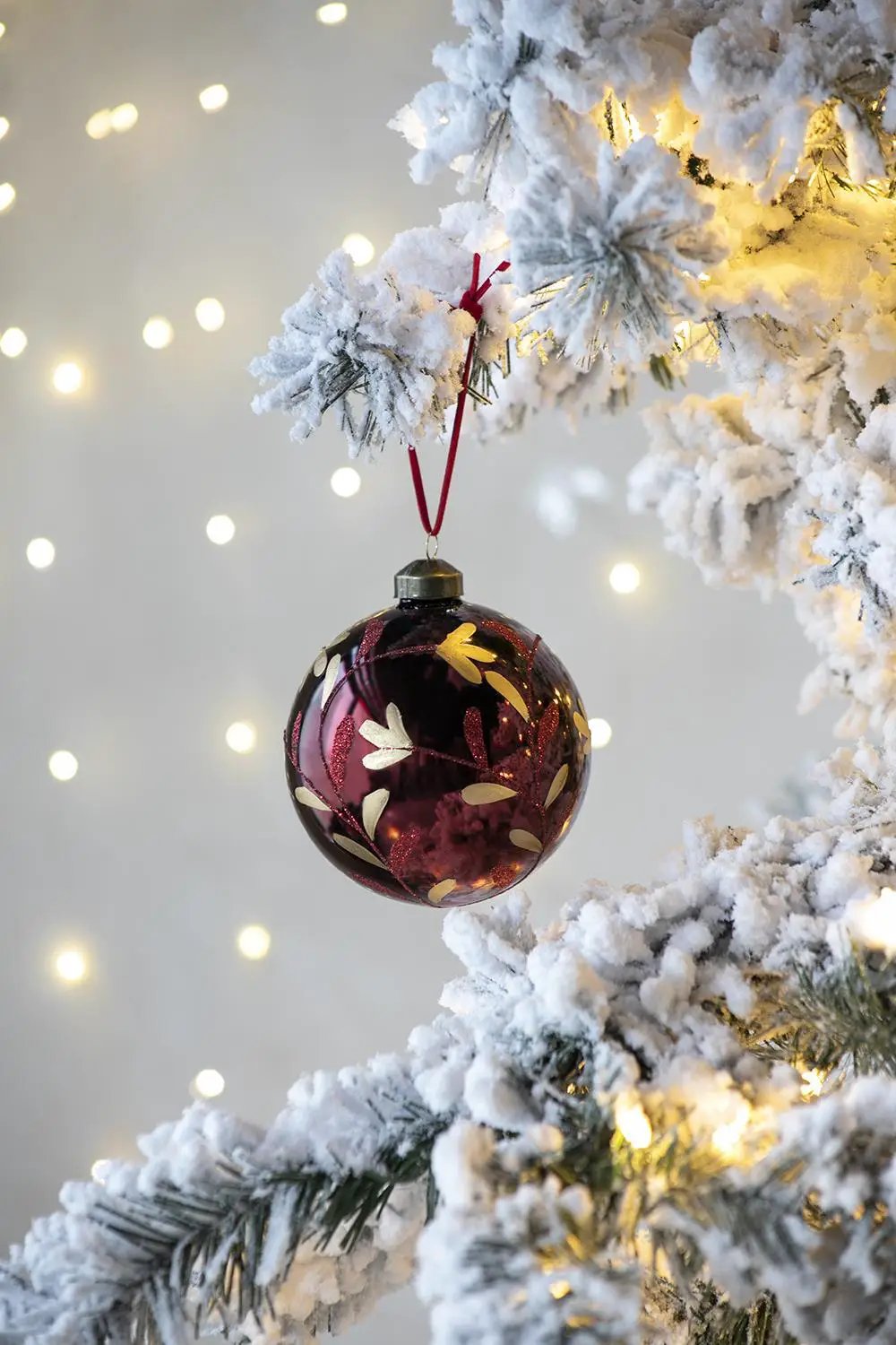 Glass burgundy Christmas ball ornament with gold leaf pattern, hanging from a snowy tree on Tampa Home & Garden Store