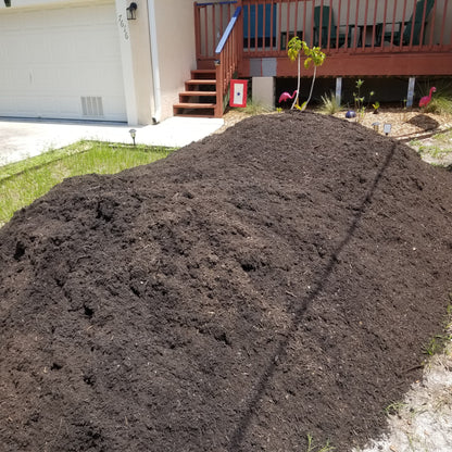 Large 9 cubic yard pile of dark brown garden soil delivered to the front yard.