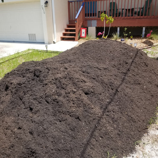 Large 9 cubic yard pile of dark brown garden soil delivered to the front yard.