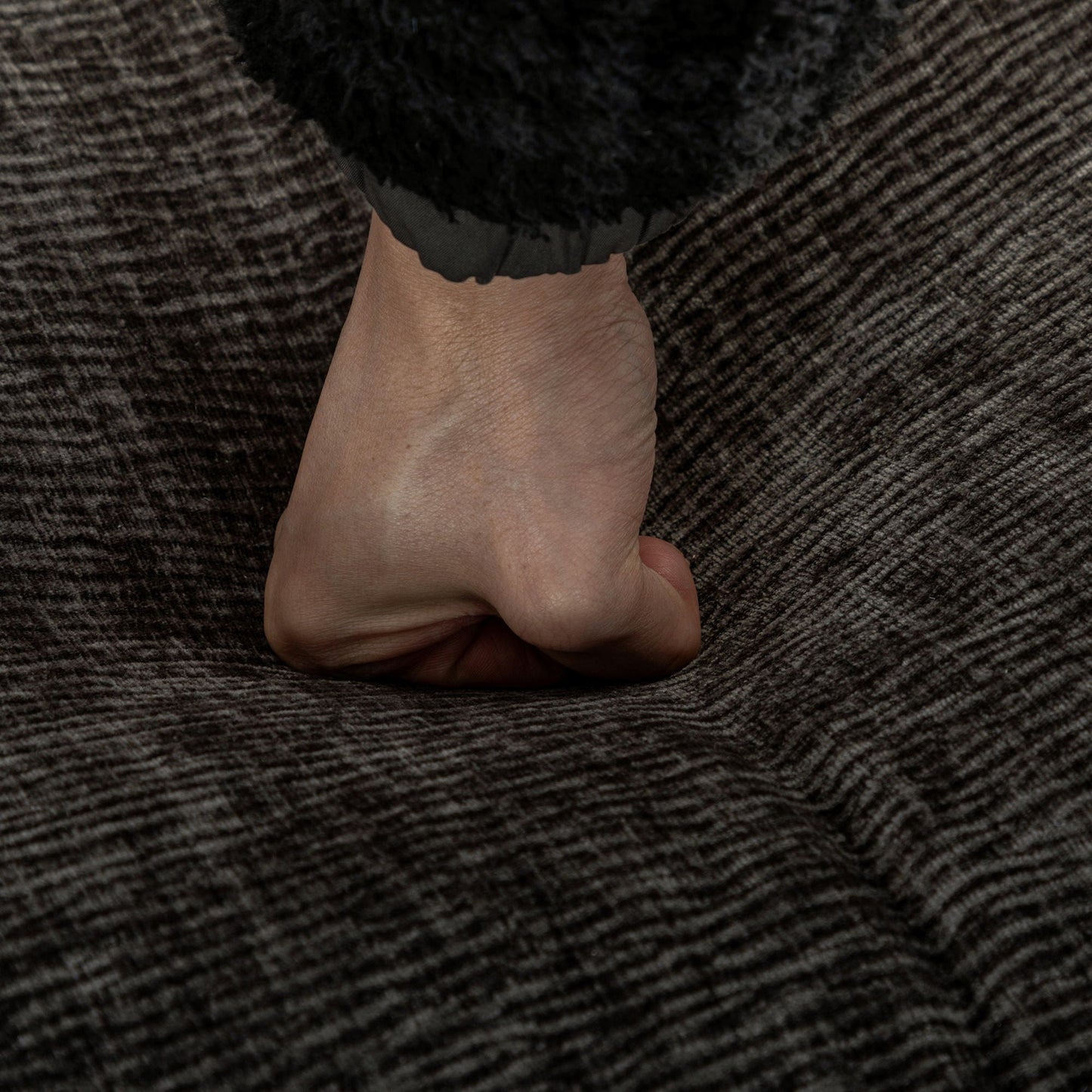 Close-up of a hand grasping a black ruffled sleeve against dark textured upholstery on Tampa Home & Garden Store