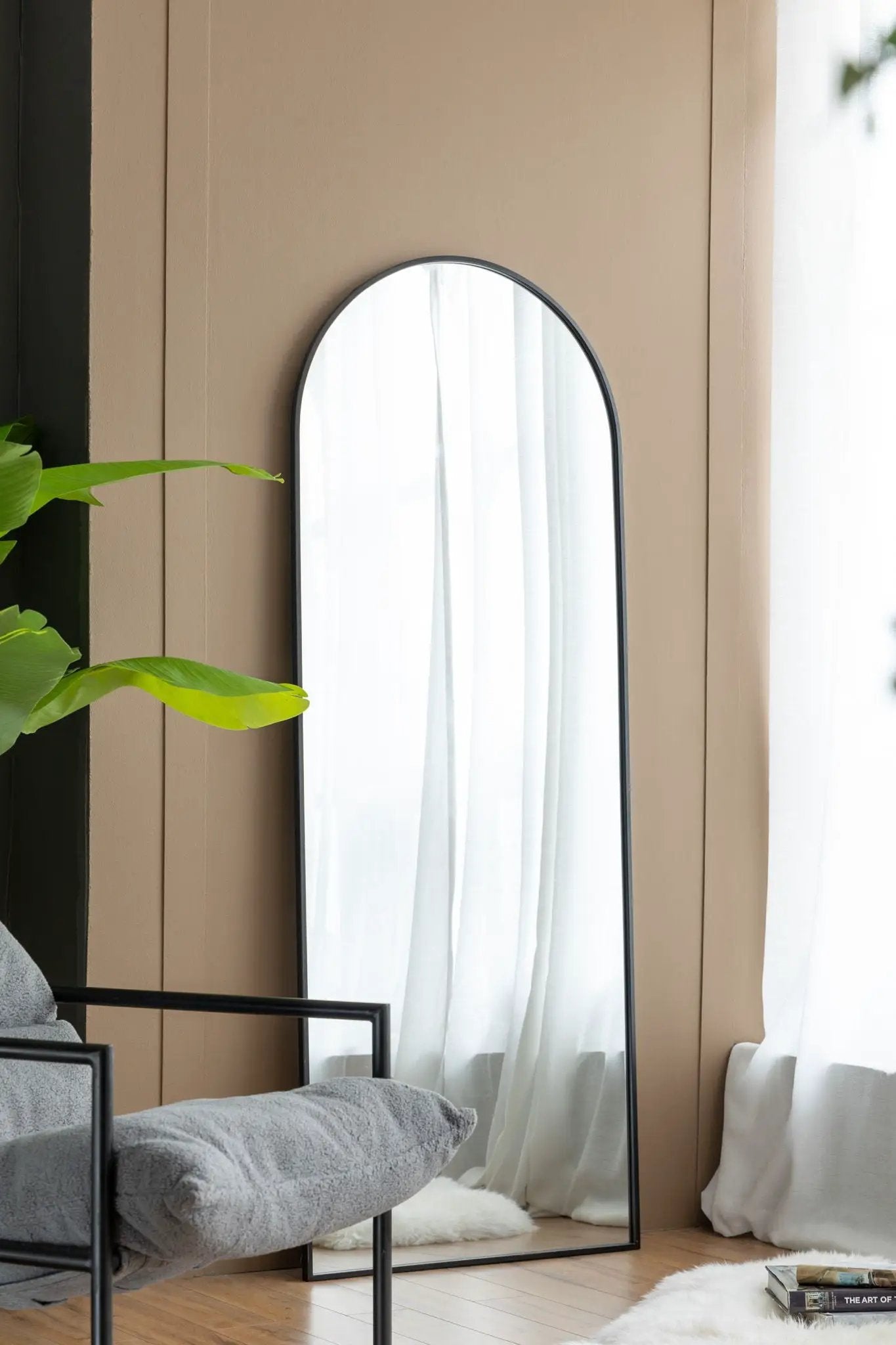 Celine Arch Body Mirror with black metal frame leaning on a tan wall by Unique Piece Furniture on Tampa Home & Garden Store