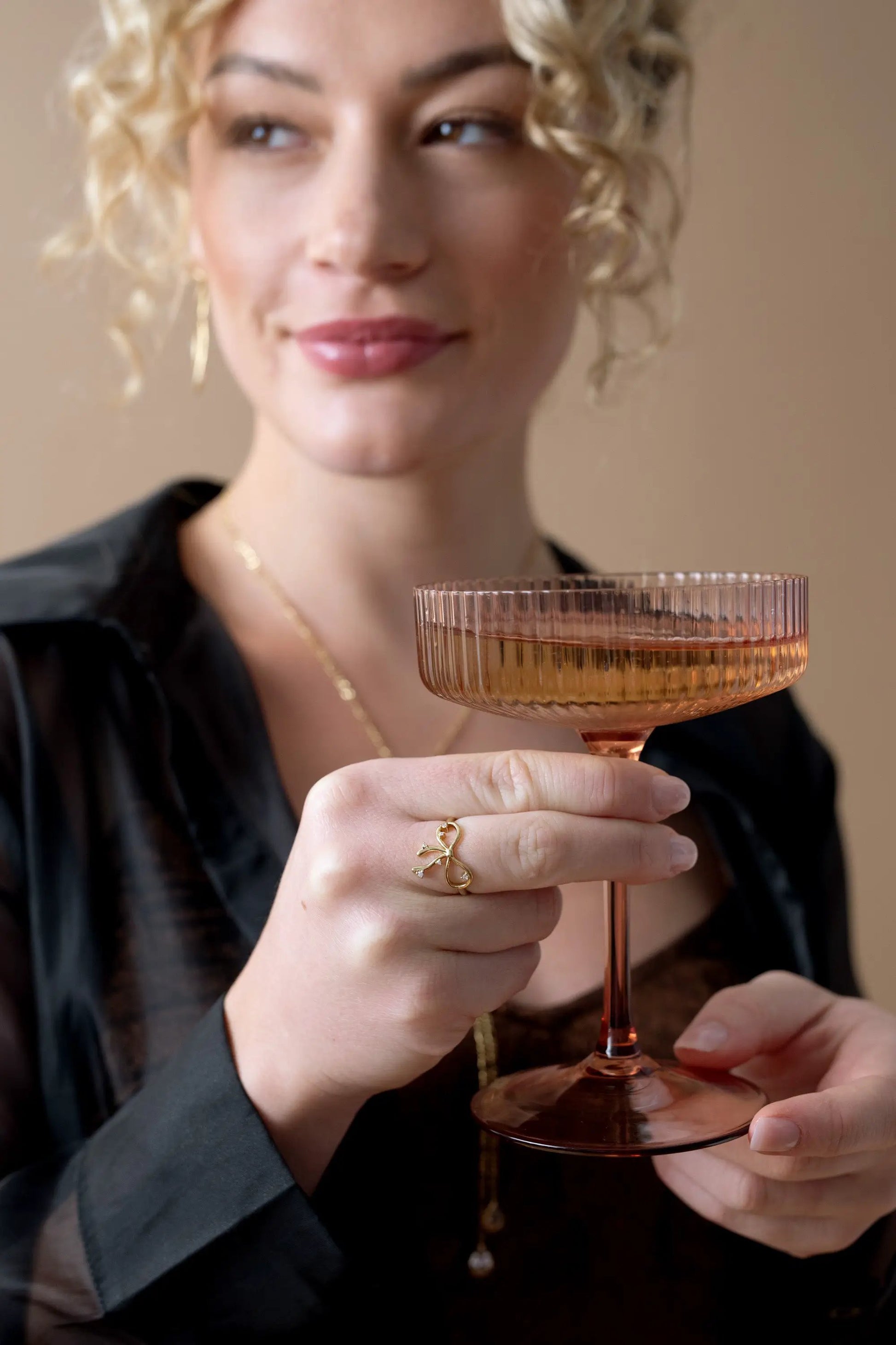 Coquette Bow Ring by Alex and Ani, goldtone bow on finger while holding a pink coupe glass on Tampa Home & Garden Store