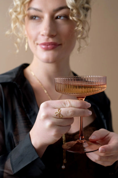 Coquette Bow Ring by Alex and Ani, goldtone bow on finger while holding a pink coupe glass on Tampa Home & Garden Store