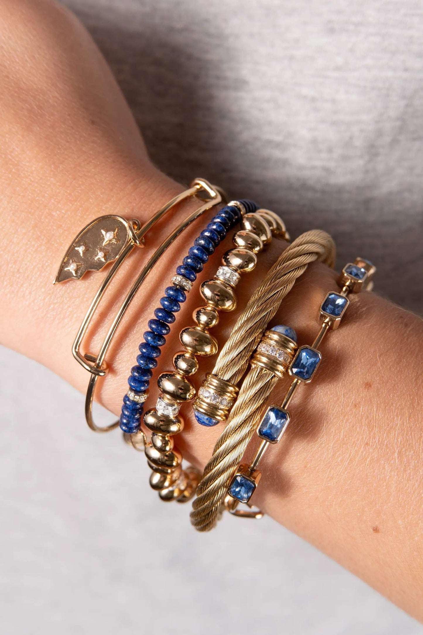 Bracelet stack: September Birthstone Emerald Cut Bangle by ALEX AND ANI in gold with blue beads on wrist on Tampa Home & Garden Store