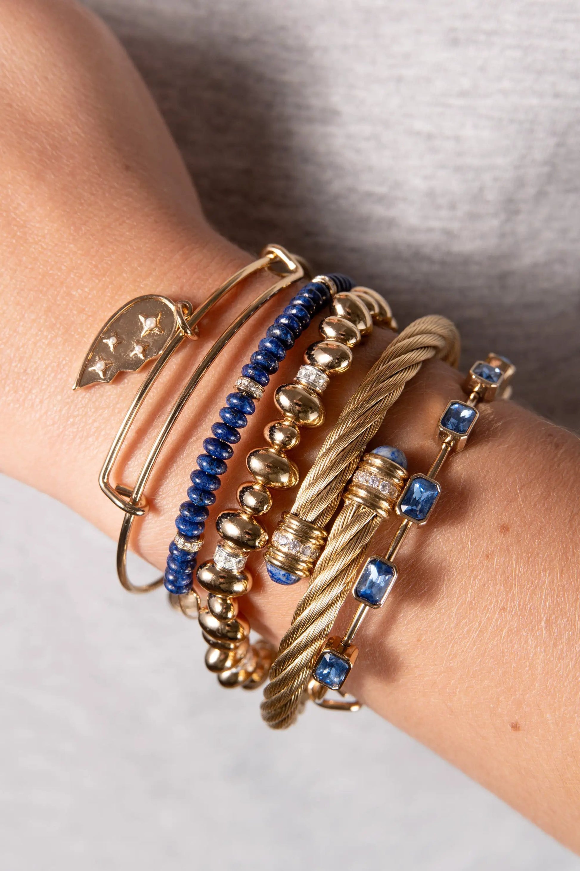 Bracelet stack: September Birthstone Emerald Cut Bangle by ALEX AND ANI in gold with blue beads on wrist on Tampa Home & Garden Store