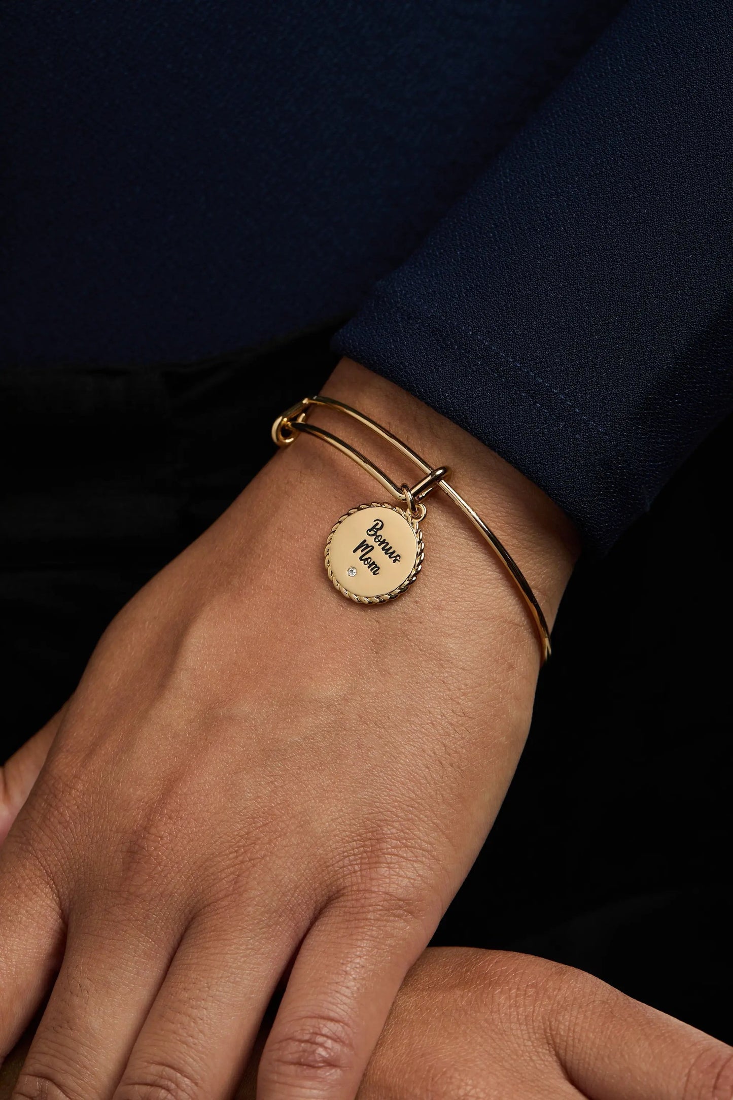 Gold-tone Alex and Ani bracelet with round 'Bonus Mom' charm on a wrist with navy sleeve on Tampa Home & Garden Store