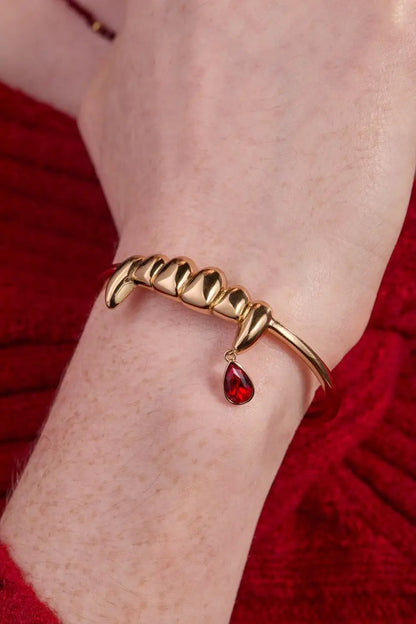 Gold-tone vampire teeth cuff bracelet by ALEX AND ANI with a red teardrop charm on wrist on Tampa Home & Garden Store