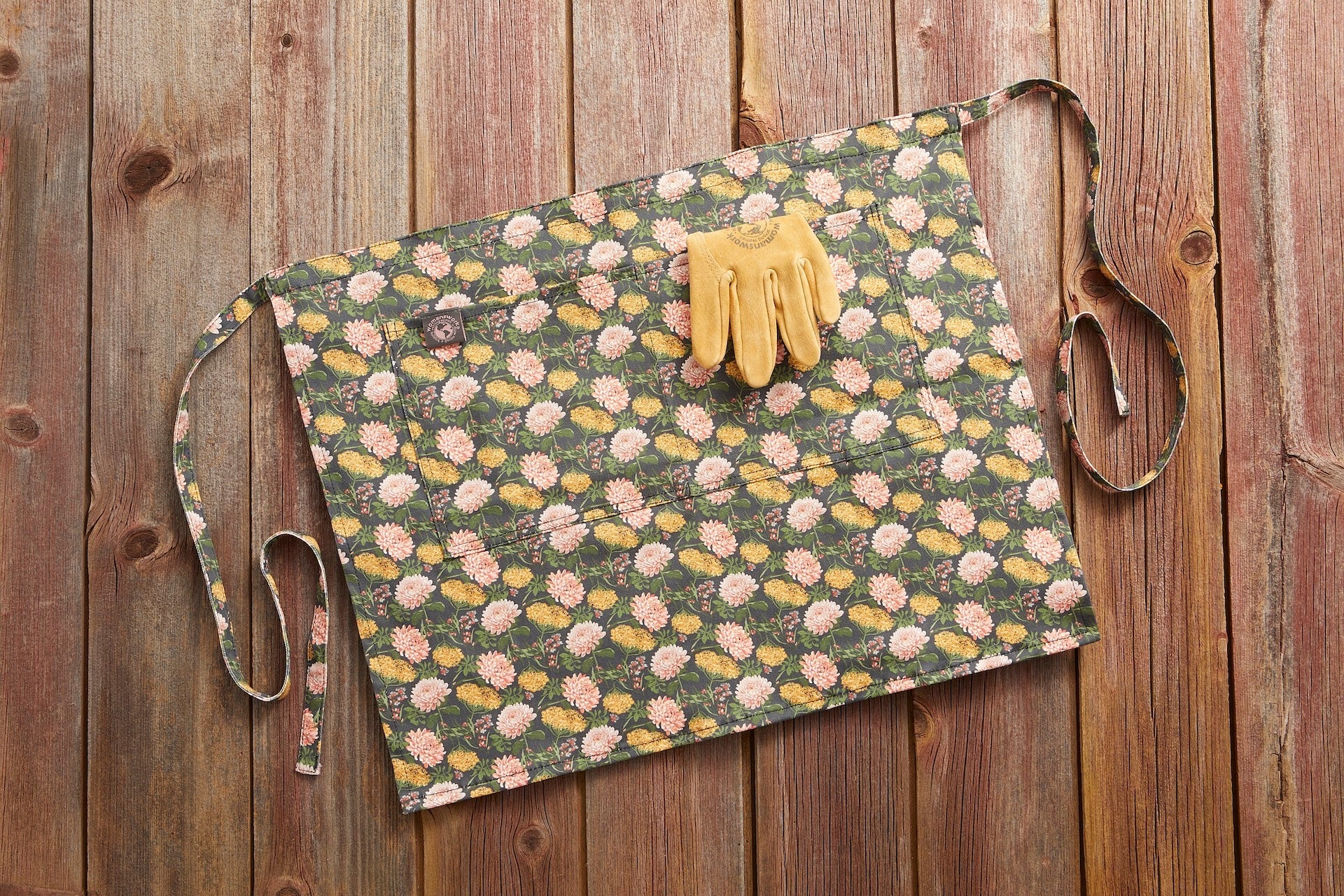 Gardener's Half Apron green floral print with pink and yellow blossoms; tan leather gloves on top on Tampa Home & Garden Store