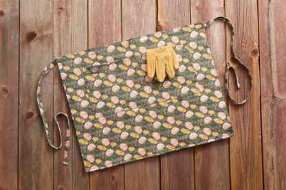 Gardener's Half Apron green floral print with pink and yellow blossoms; tan leather gloves on top on Tampa Home & Garden Store