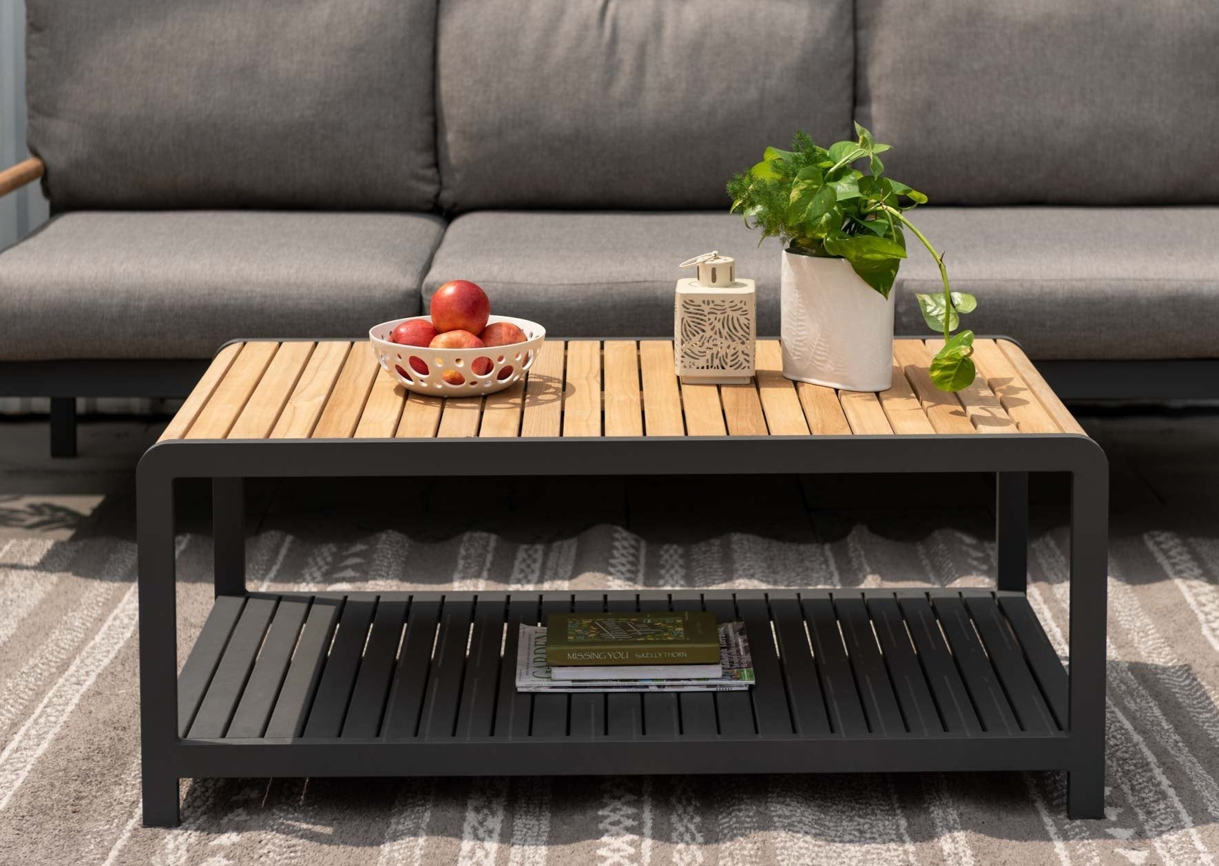 Amber teak and aluminum coffee table with slatted top; fruit bowl, lantern, trailing plant on Tampa Home & Garden Store