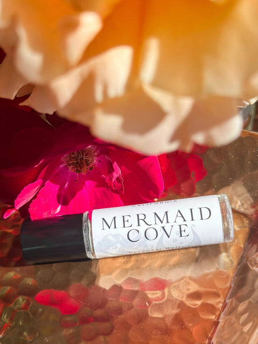 Perfume oil Mermaid Cove Aquatic Green Fresh in a clear roller bottle among pink flowers on Tampa Home & Garden Store