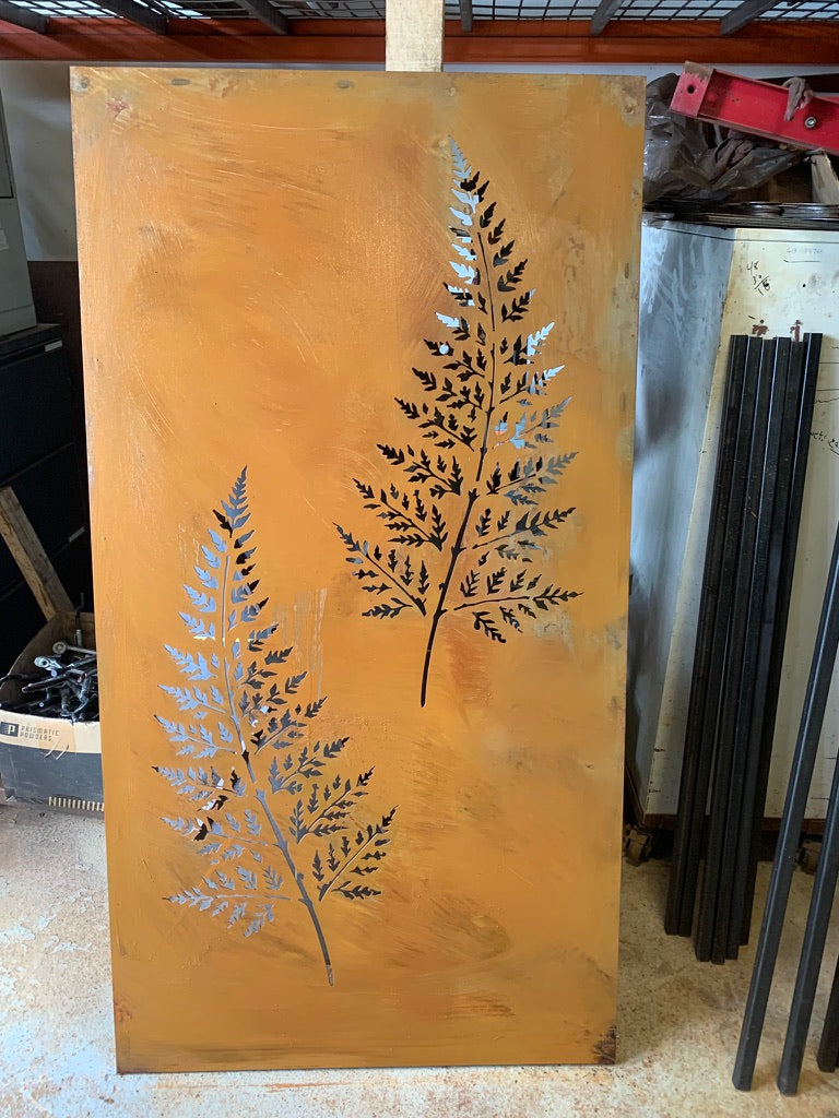 Outdoor metal privacy panel with two fern leaf cutouts in dark steel on copper patina background on Tampa Home & Garden Store