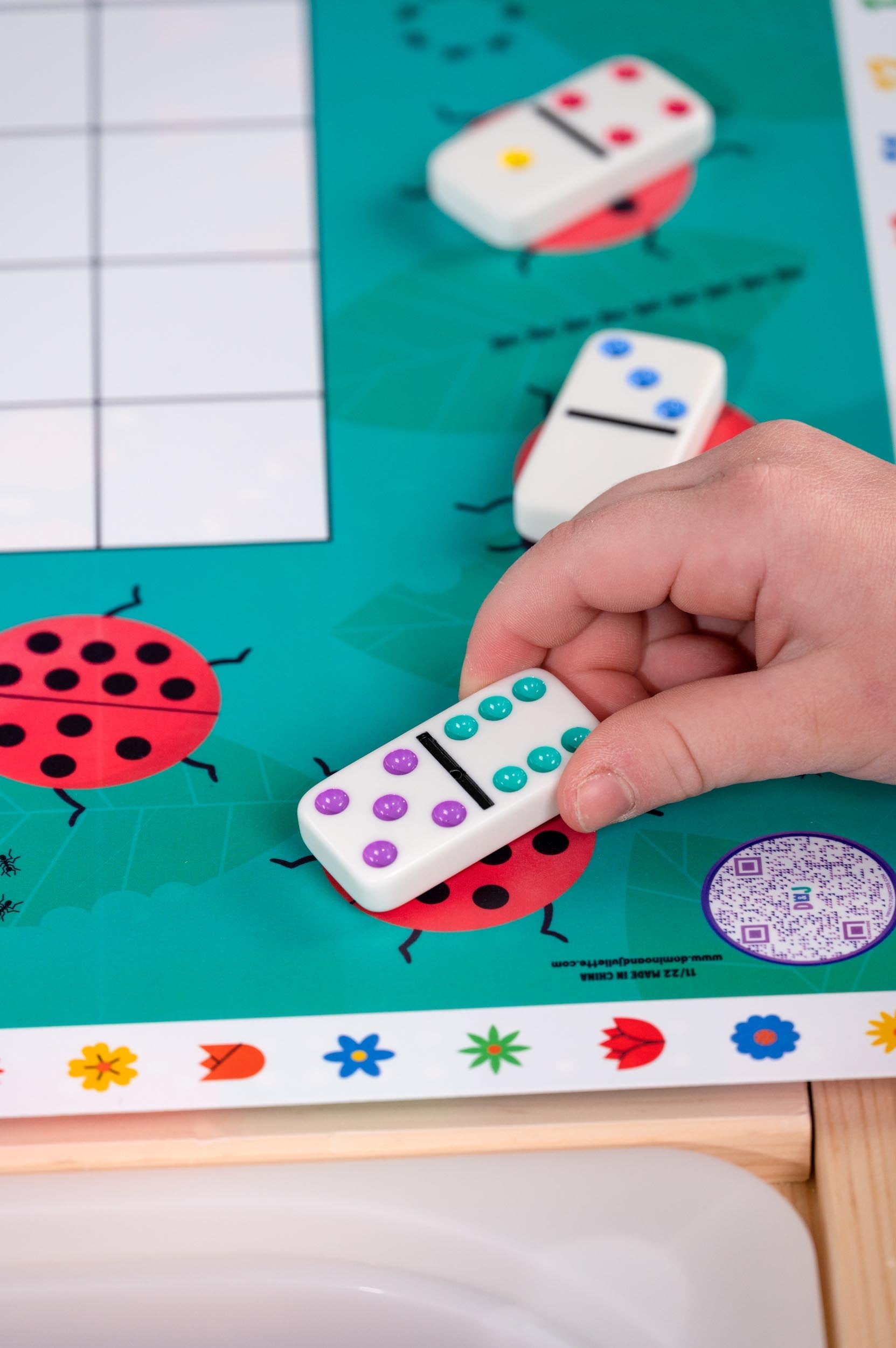 Bright Play Dominos, two white tiles with purple and teal pips, on teal game board with ladybugs on Tampa Home & Garden Store